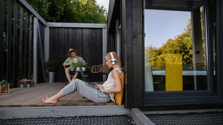 Zwei Personen sitzen auf der Terasse ihres Hauses. Während die Frau am Laptop arbeitet, liest der Mann ein Buch.