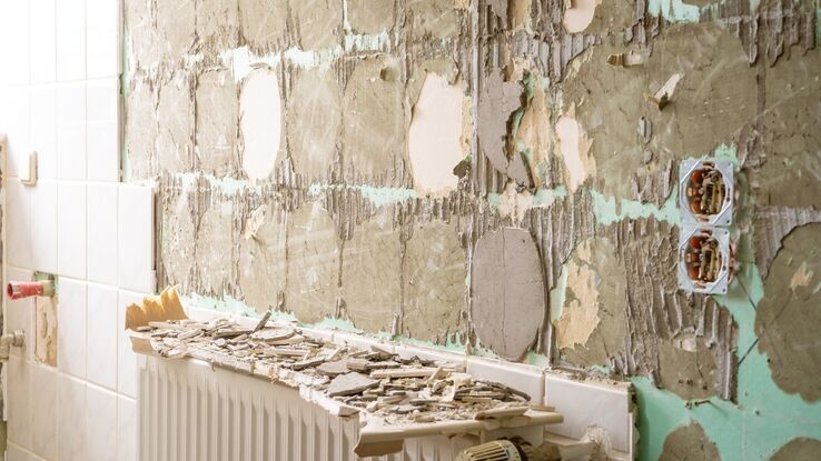 Es ist eine Wand abgebildet, von der die Fliesen abgemacht wurden. Auf der Heizung liegen die Überreste. Hinten ist noch ein Teil der Fliesen an der Wand zu sehen.