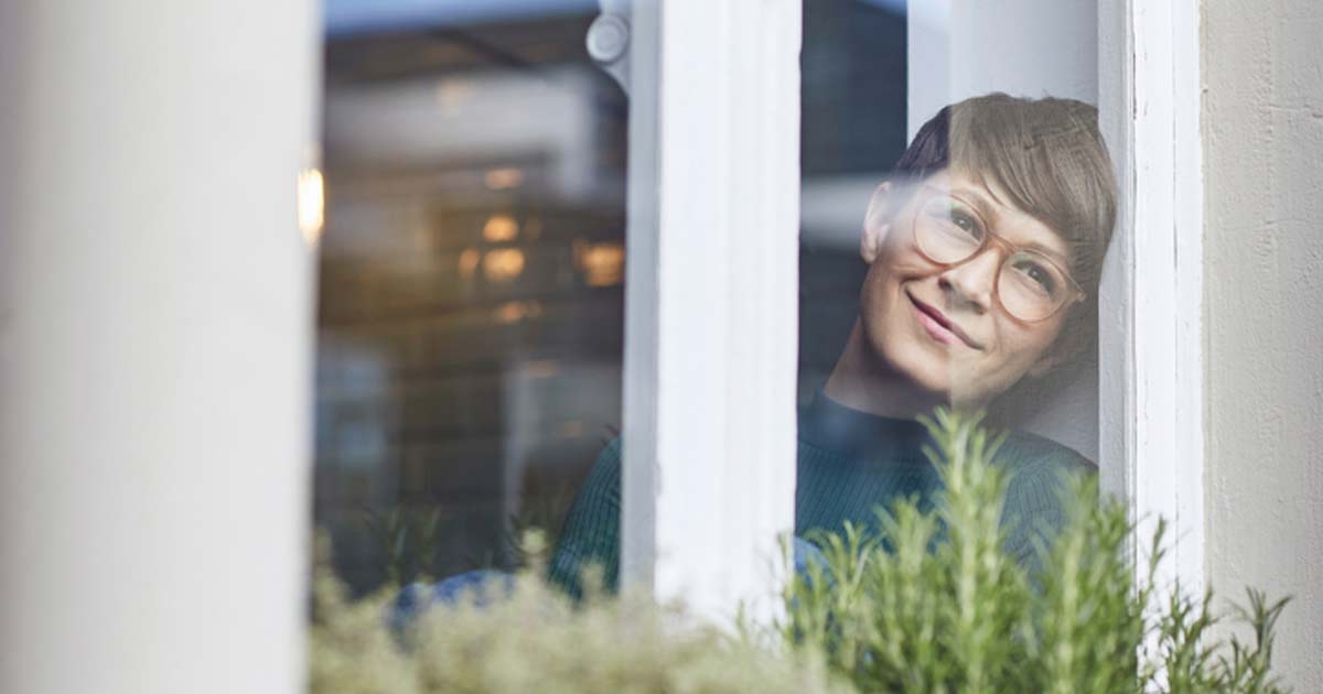 Eine frau mit Brille blickt lächelend durch eine Scheibe in ihren Garten.