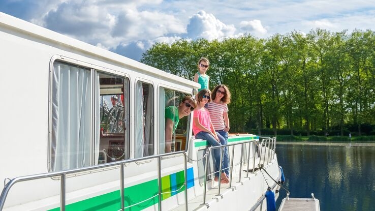 Das Foto zeigt eine Familie auf einem Hausboot. Es sind Mutter, Vater und zwei Töchter zu erkennen. Das Hausboot liegt aktuell an einem Steg.
