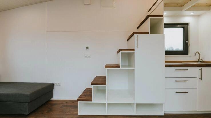 Das Foto zeigt ein Treppenregal. Es führt über die Küchenzeile in die obere Etage. Unter der Treppe befindet sich ein Regal und die Küchenzeile.