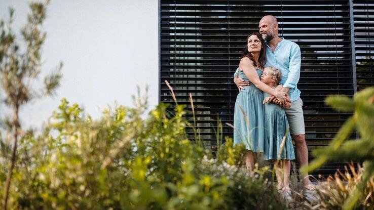 Eine kleine Familie steht Arm in Arm vor ihrer Immobilie.