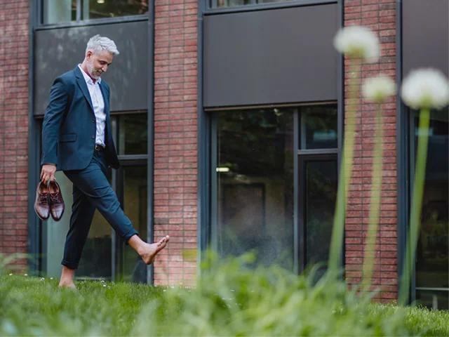 Person läuft barfuß vor einem modernen Gebäude und trägt Schuhe in der Hand.