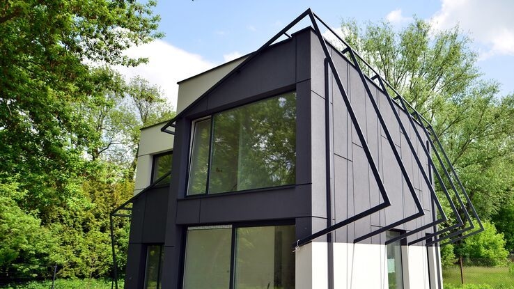 Abgebildet ist ein Haus im ganz speziellen Baustil mit schönem grünen Garten.