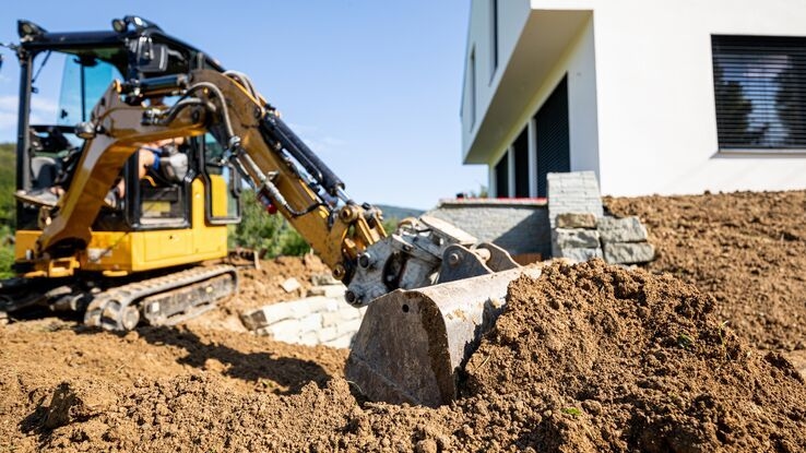 Man sieht eine Baustelle mit einem Bagger im Vordergrund und dem Eigenheim im Hintergrund.
