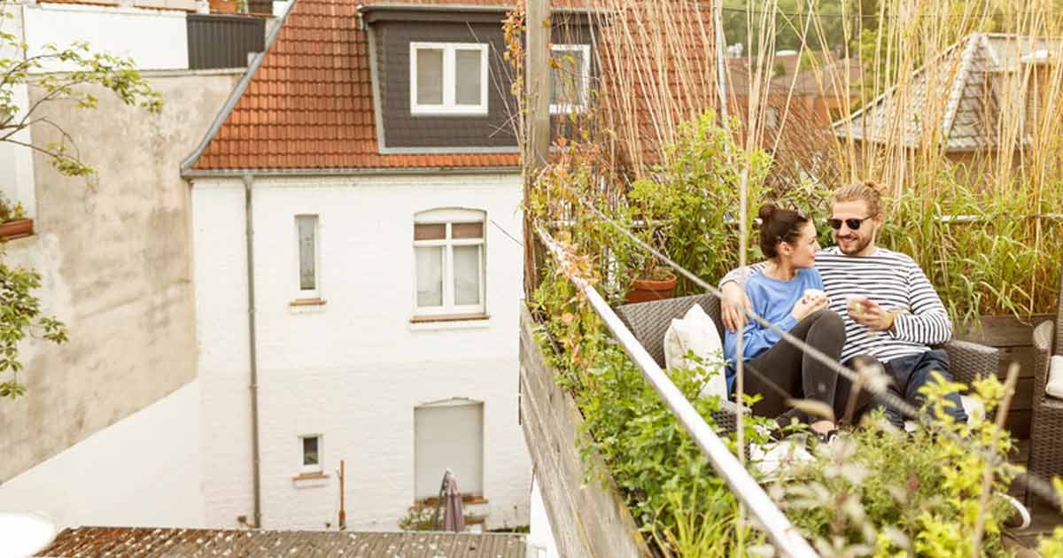 Ein Paar sitzt auf einem Balkon umgeben von Pflanzen und trinkt Kaffee.
