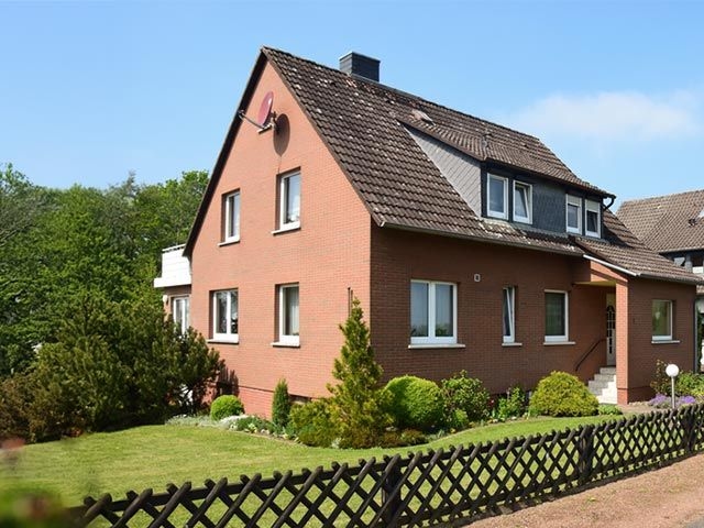 Zu sehen ist ein Einfamilienhaus mit Garten daneben und einem Zaun drum herum.