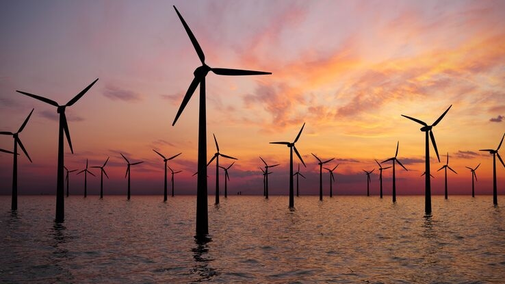 Es stehen viele Windräder im Meer bei Sonnenuntergang.