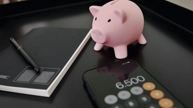 Ein Smartphone kalkuliert die Kosten. Ein Sparschwein symbolisiert den Bausparvertrag.