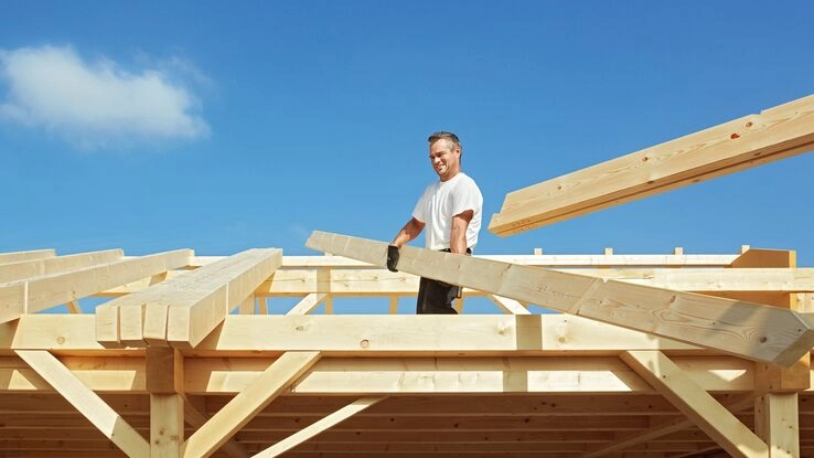 Auf dem Bild sieht man einen Mann beim Bau von einem Dachstuhl.