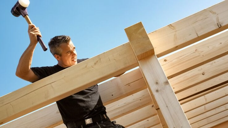Ein Handwerker macht den Dachstuhl fertig. Nur noch wenige Schritte bis zum Richtfest.