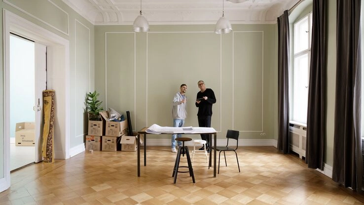 Ein Altbau mit hohen Wänden. Der Raum ist nahezu leer und zwei Personen planen den Einzug.