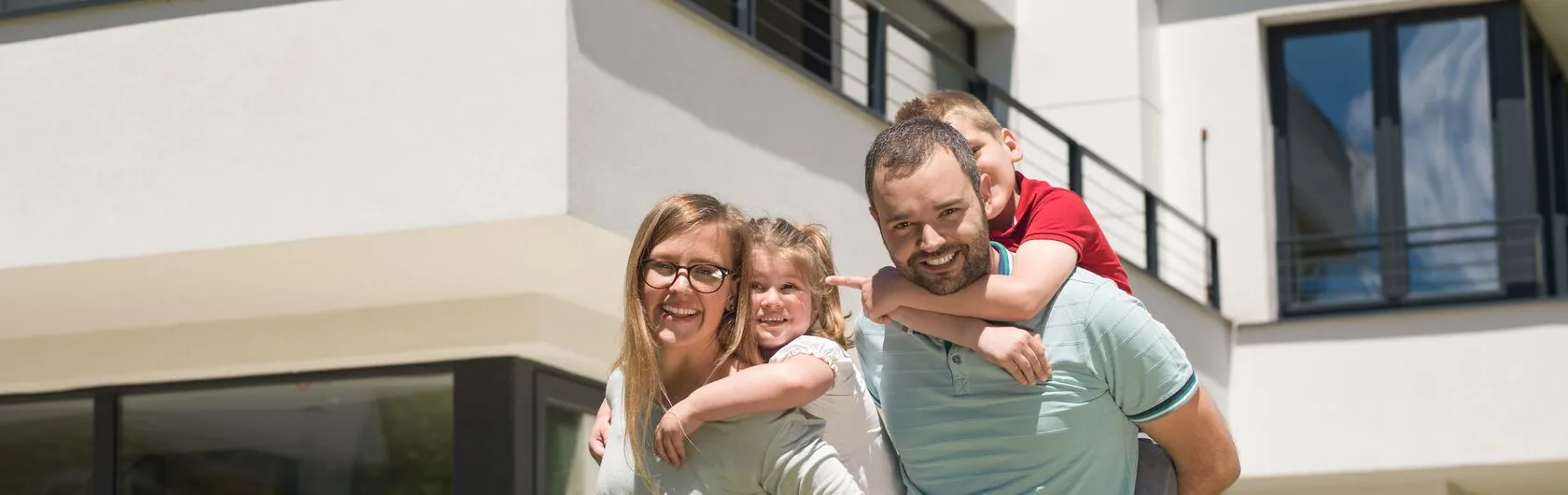 Eine junge Familie steht vor einer Immobilie, die sie im nächsten Augenblick besichtigen werden.