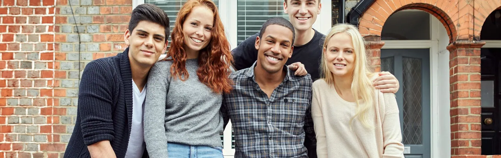 Fünf junge Personen stehen vor einer Immobilie. Sie leben in einer WG zusammen.