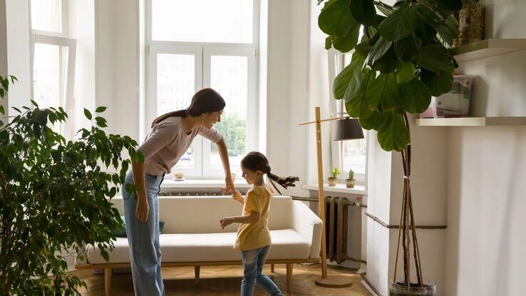 Eine Frau tanzt mit ihrer Tochter im Wohnzimmer.