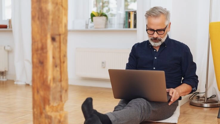 Ein Mann sitzt auf dem Boden, mit einem Laptop auf dem Schoß.