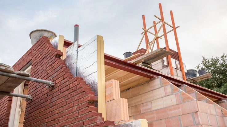 Das Foto zeigt ein Haus im Aufbau. Zwischen Außenwand und Innenwand des Hauses schaut eine Dämmplatte hervor.