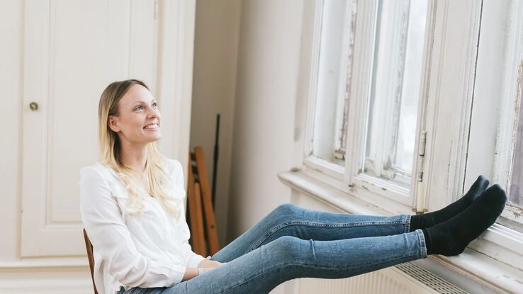 Symboldbild für das KfW-Programm 358/359: Eine Frau wirkt zufrieden und schaut aus dem Fenster.