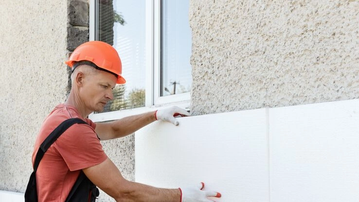 Ein Handwerker bringt an der Außenfassade die Dämmung an.