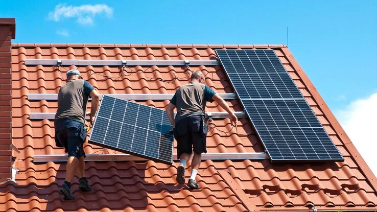 Zwei Personen installieren eine Photovoltaikanlage auf dem Dach. Dabei ist einiges zu beachten.