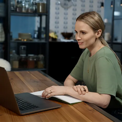 Eine Frau informiert sich am Laptop und hat ein Notizbuch vor sich.