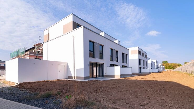 Neugebaute Häuser mit weißer Außenfassade. Der Garten ist noch Baustelle.