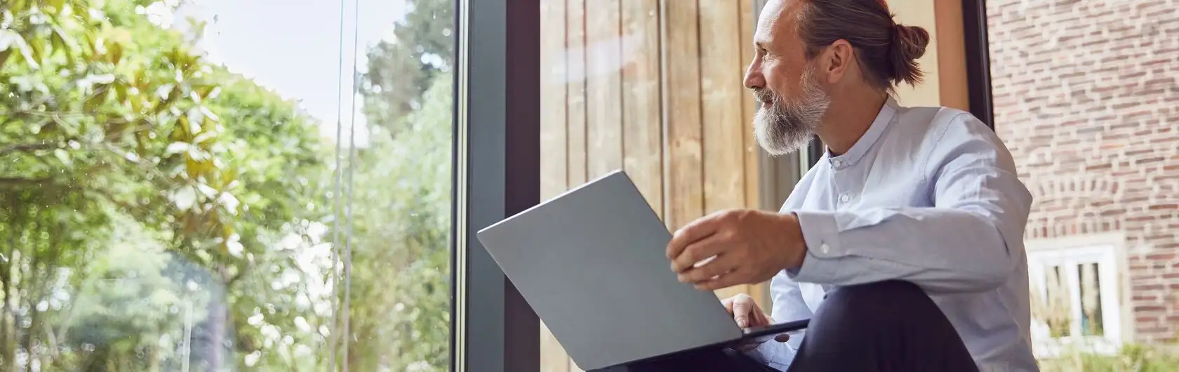 In Mann blickt in den Garten und erstellt an seinem Laptop ein Immobiliengutachten.