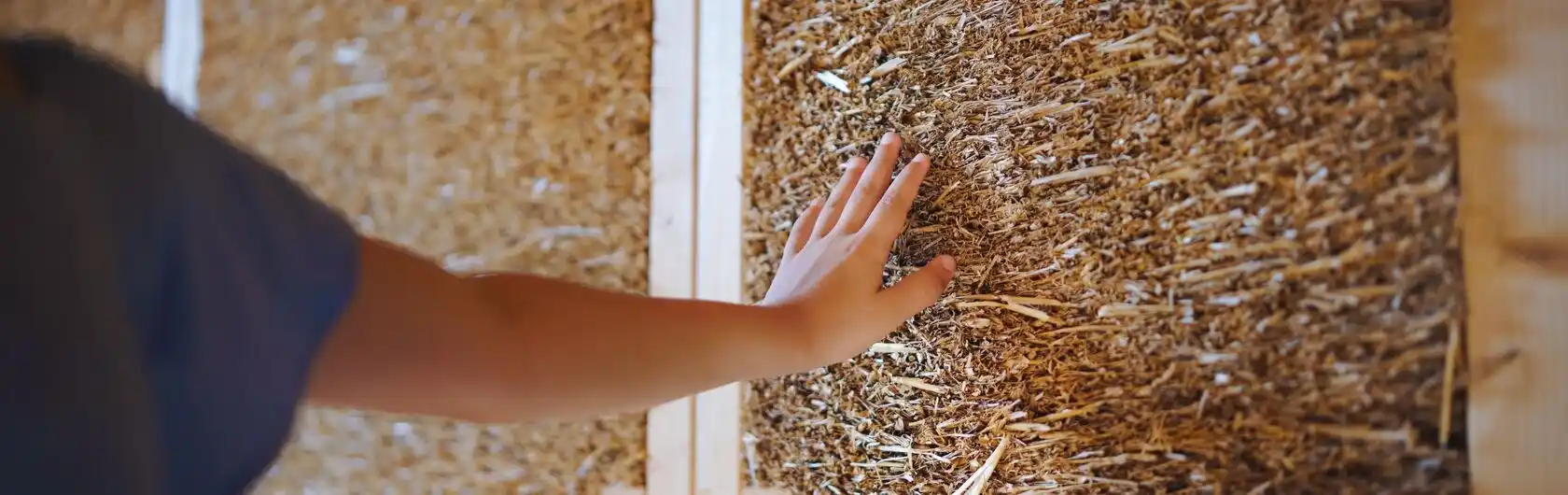 Eine Kinderhand streicht über eine Wand aus Stroh.