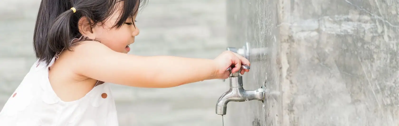 Wasser und Strom sparen ist wichtig. Ein kleines Kind macht es vor, indem es einen Wasserhahn zudreht.