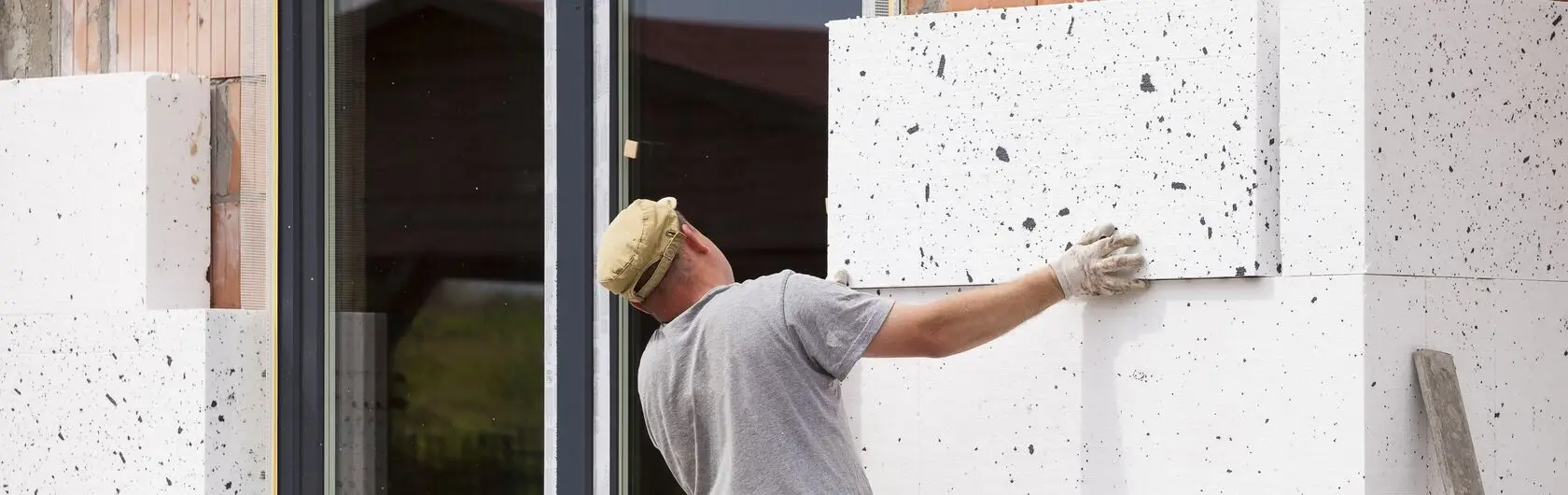 Ein Handwerker bringt an einem Haus Dämmstoff-Platten an.
