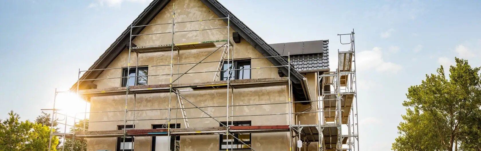 Das Bild zeigt ein Haus, welches mit von einem Baugerüst umgeben ist. Es zeigt eine anstehende Fassadensanierung.