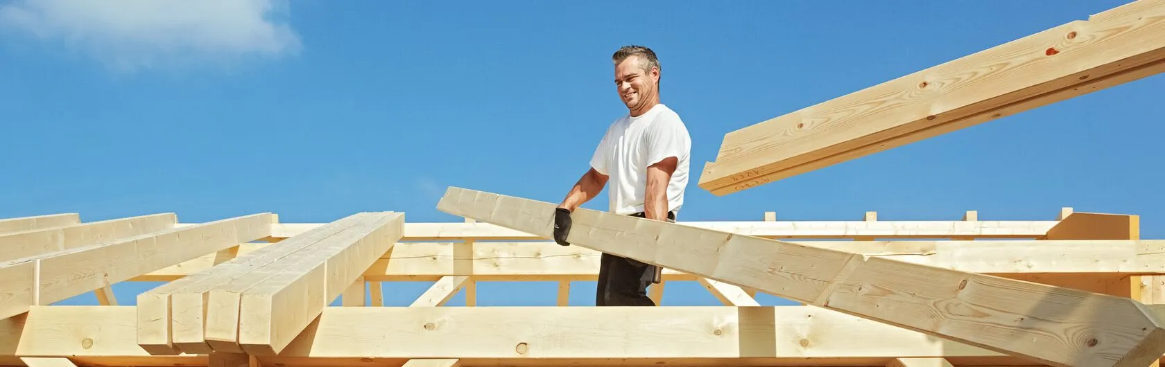 Ein Bauarbeiter trägt Holzbalken auf einer Baustelle.