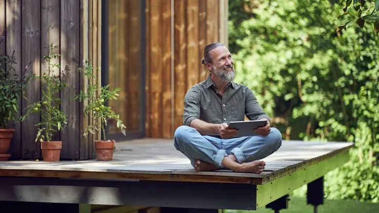 Ein Mann sitzt auf seiner Terrasse auf dem Boden und liest ein Buch.