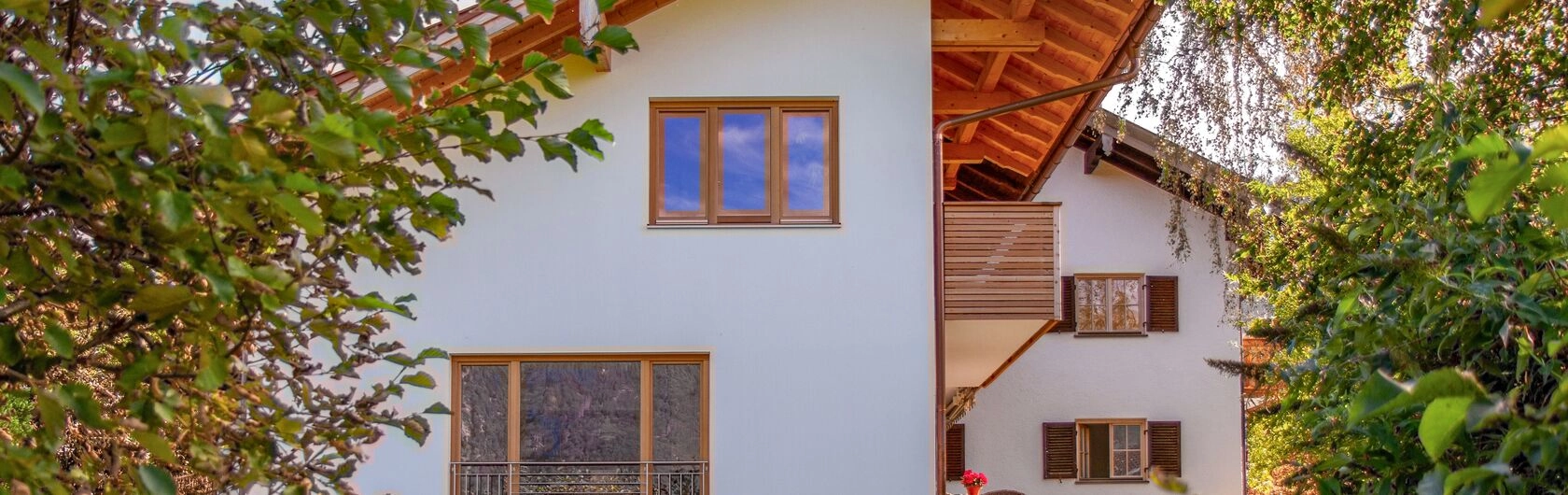 Man sieht ein Haus mit modernen Fenstern und Balkon aus Holz.