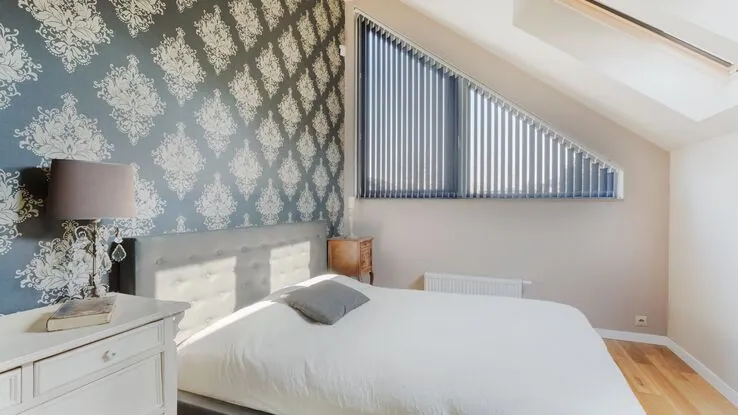 Ein modernes Schlafzimmer im Dachgeschoss mit einem großen Bett und einer graphischen Tapete als Betthintergrund