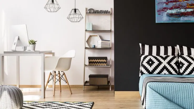 Ein schwarz-weiß gestaltetes Zimmer mit einem Bett vor einer schwarzen Wand und einem Schreibtisch.