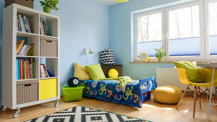 Ein hellblaues Kinderzimmer mit einem bunt dekorierten Kinderbett und einem Bücherregal.