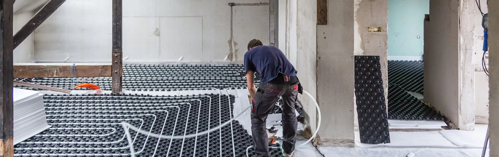Eine Immobilie wird saniert und ein Handwerker rüstet eine Fußbodenheizung nach.