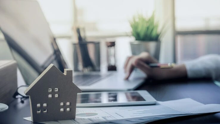 Das Foto steht sinnbildlich für das Thema Steuern bei einem Immobilienverkauf und zeigt eine Hand an einem Laptop mit einem Haus davor.