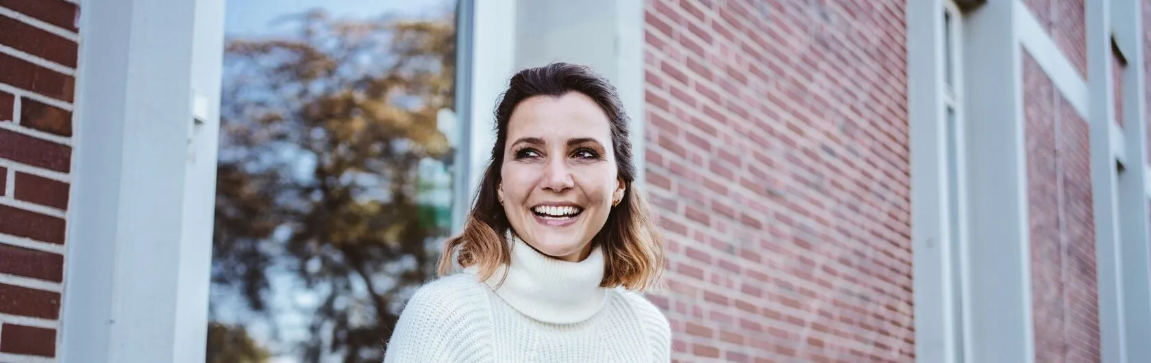 Eine Frau lächelt und sitzt stolz vor ihrer eigenen Immobilie.
