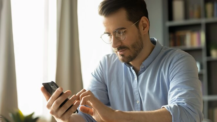 Ein Mann mit Brille errechnet die Mietrendite an seinem Smartphone.