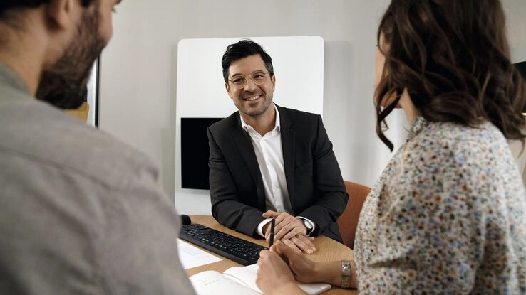 Ein Berater bespricht mit zwei Personen eine mögliche Kapitalanlage in Immobilien.