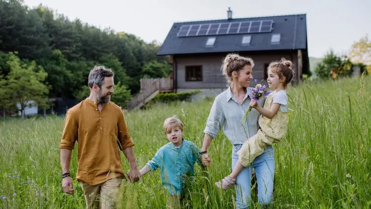 Eine Familie auf einem Feld. Im Hintergrund ist ein aus Holz gebautes Haus.