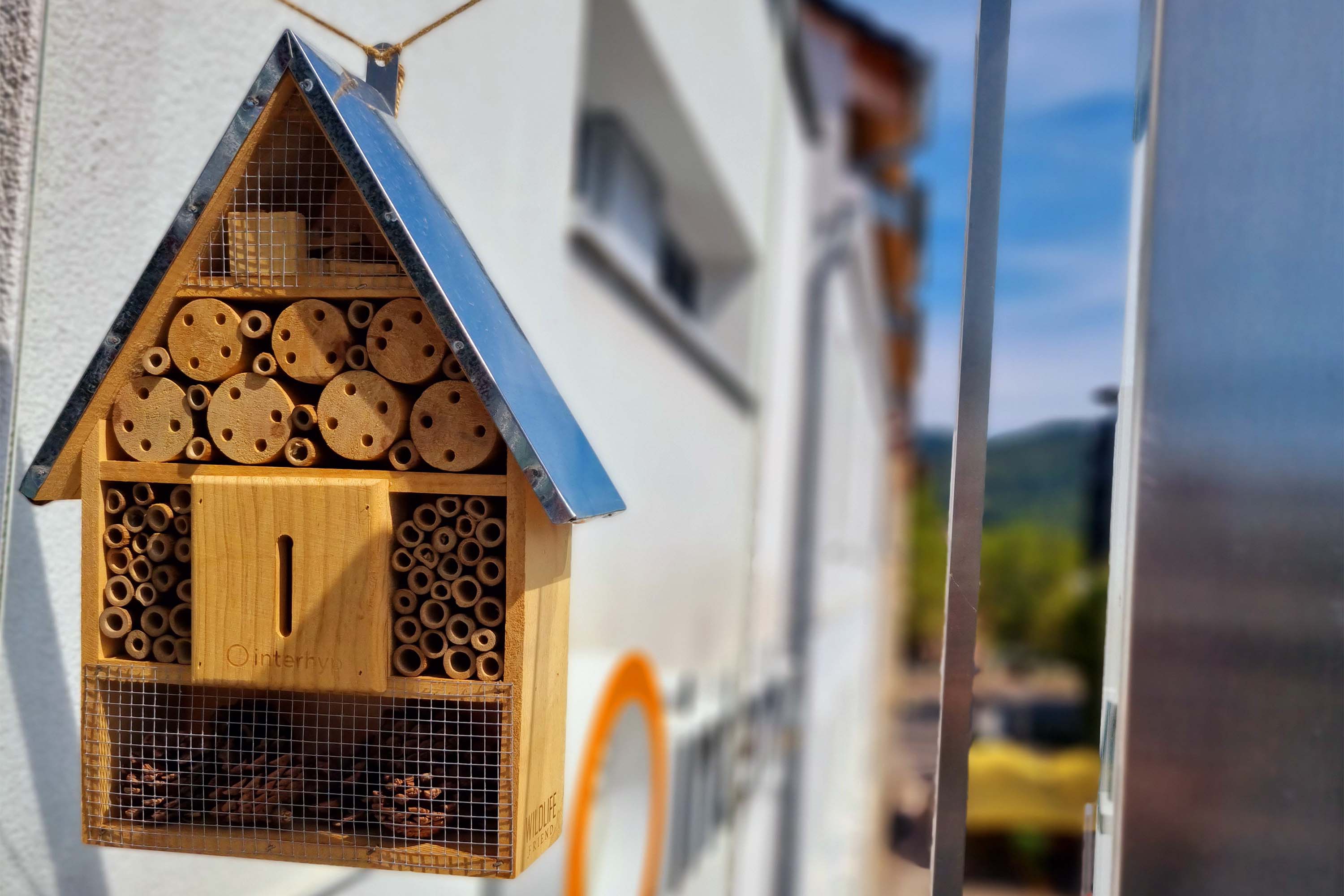 Ein Insektenhotel hängt vor einer Interhyp-Niederlassung. Im Hintergrund sieht man das Logo der Interhyp AG.