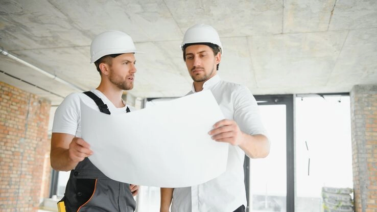 Zwei Handwerker stehen in einem Rohbau und sprechen zur Bauplanung und Vermessung.