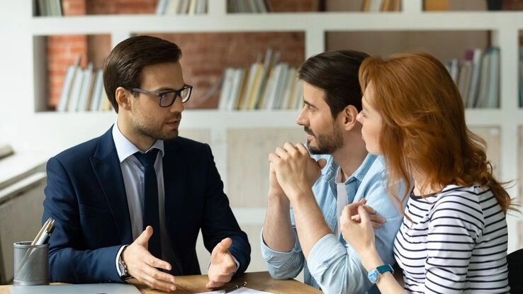 Ein Berater erklärt einem jungen Pärchen die Finanzierungsmöglichkeiten.